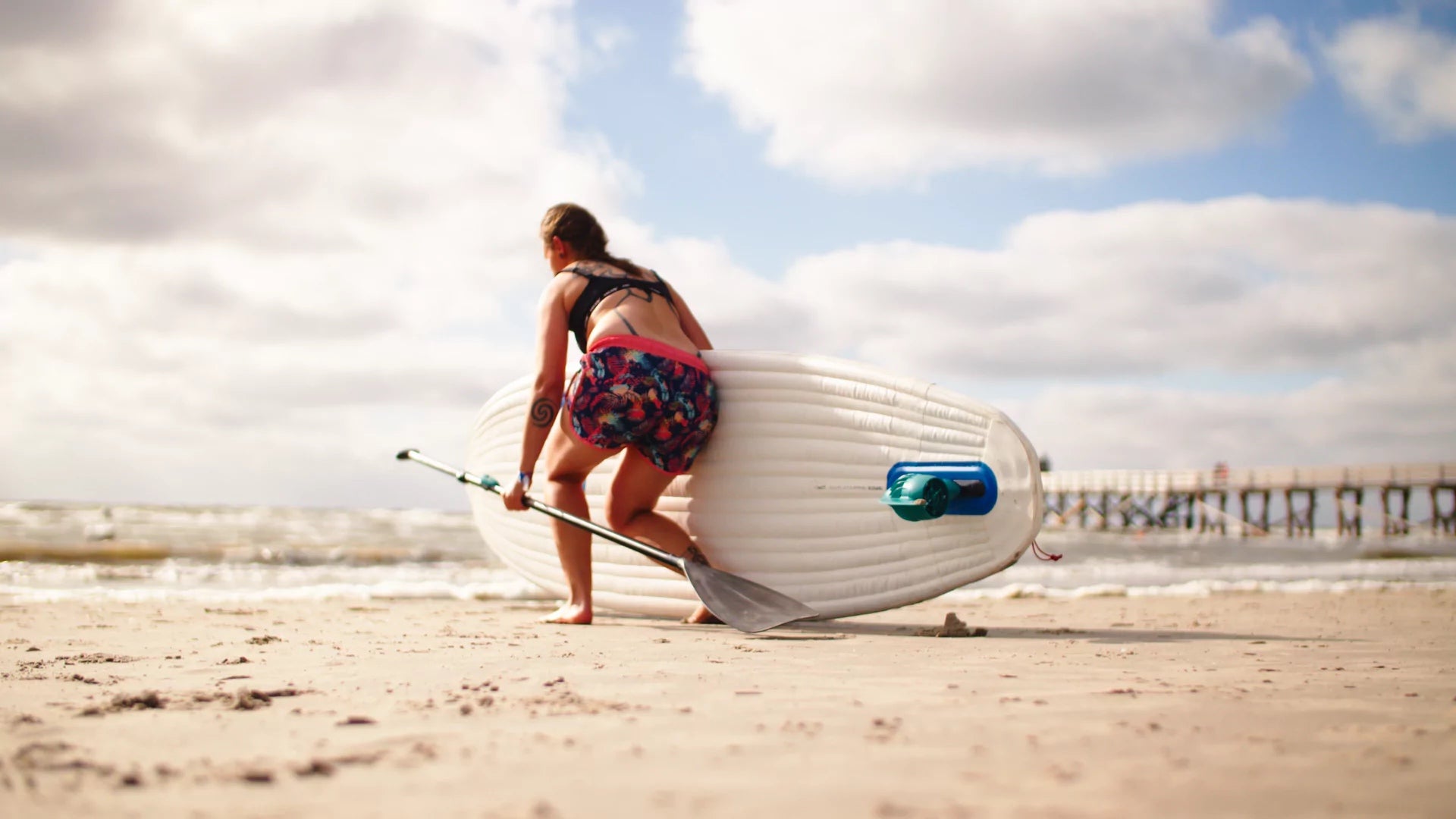 Frau trägt SUP-Board mit Elektro Finne am Strand
