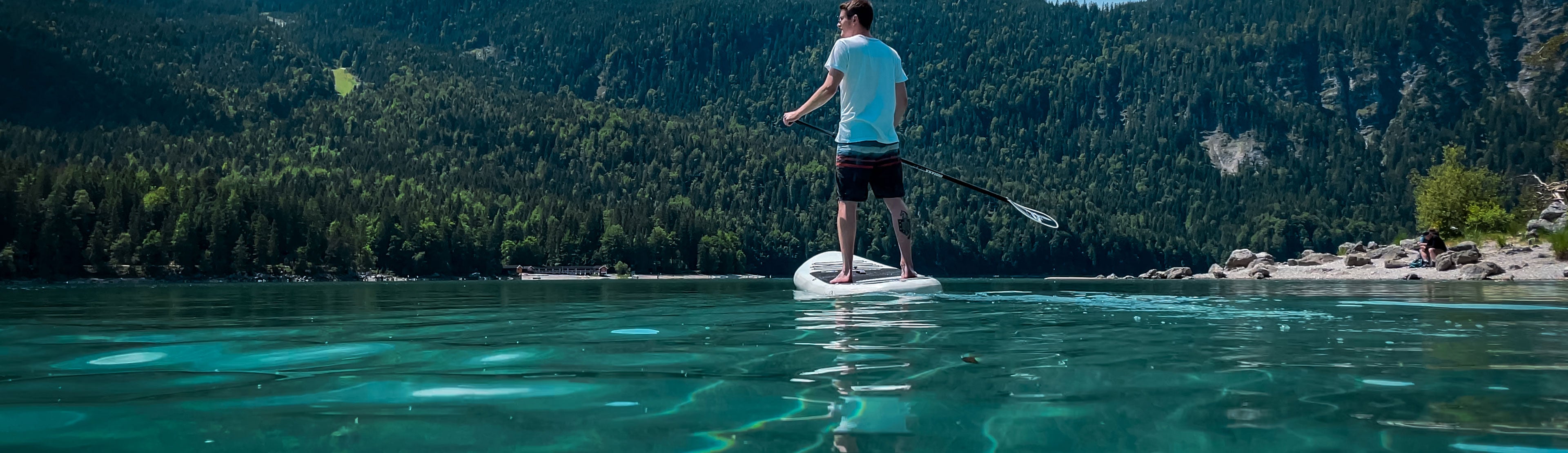 Mann steht auf SUP-Board auf Wasser